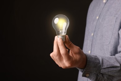 Glow up your ideas. Closeup view of man holding light bulb on black background, space for text