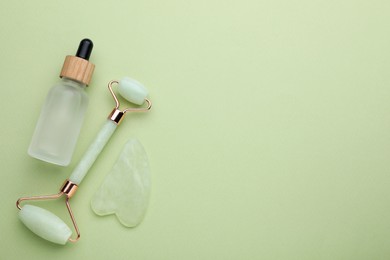 Jade gua sha tool , facial roller and bottle of serum on light green background, flat lay. Space for text