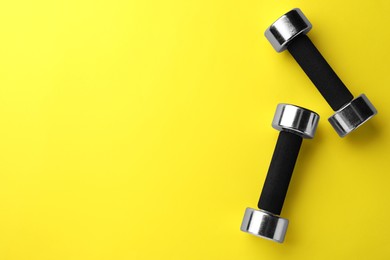 Stylish dumbbells on yellow background, flat lay. Space for text