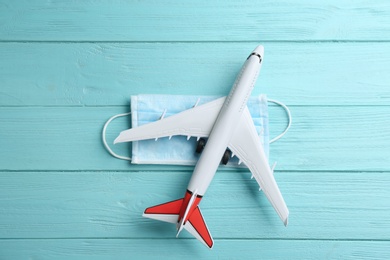 Photo of Toy airplane and medical mask on light blue wooden background, flat lay. Travelling during coronavirus pandemic