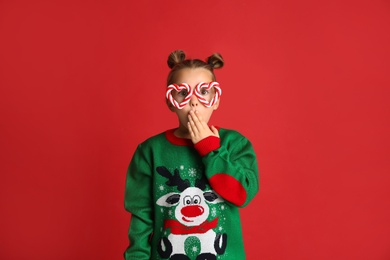 Surprised little girl in Christmas sweater and party glasses on red background