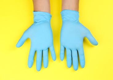 Person in blue latex gloves against yellow background, closeup on hands
