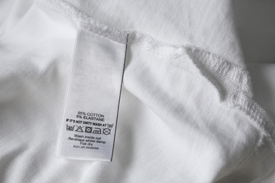 Clothing label with care symbols and material content on white shirt, closeup view