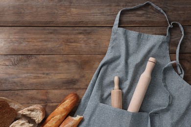 Clean kitchen apron with rolling pins and different types of bread on wooden table, flat lay. Space for text