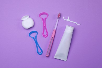 Flat lay composition with tongue cleaners and teeth care products on violet background