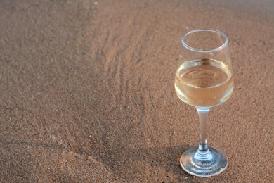 Photo of Glass of tasty wine on wet sand, space for text