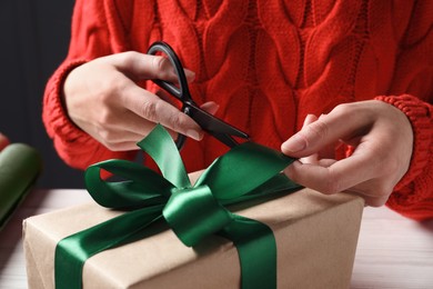 Christmas present. Woman decorating gift box at table, closeup