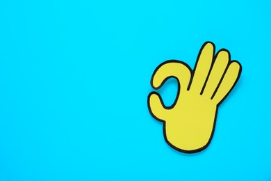 Photo of Paper cutout of okay hand gesture on light blue background, top view. Space for text