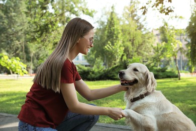 Cute golden retriever dog giving paw to young woman in park