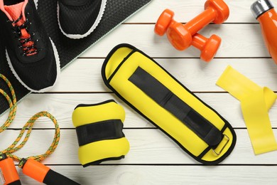 Yellow weighting agents and sport equipment on white wooden table, flat lay