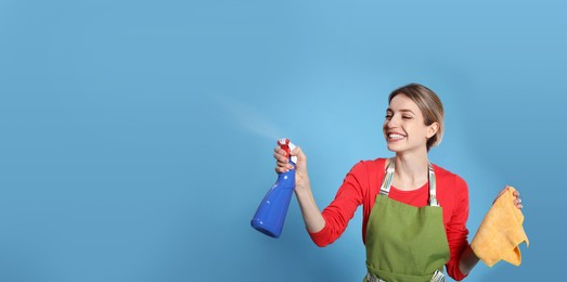 Photo of Young housewife with detergent and rag on light blue background
