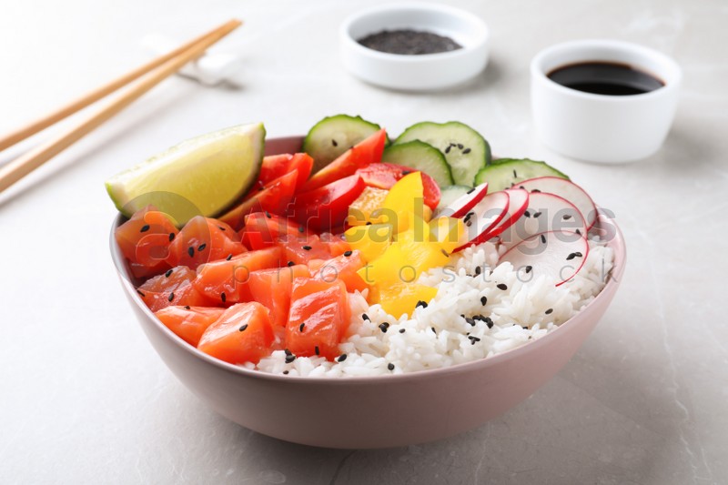 Delicious poke bowl with salmon, rice and vegetables served on light grey table