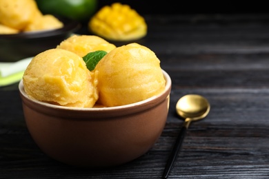 Yummy mango ice cream in bowl on black wooden table. Space for text