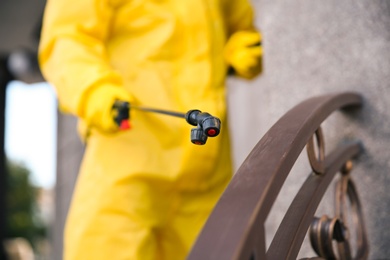 Person in hazmat suit disinfecting railing, focus on sprayer. Surface treatment during coronavirus pandemic
