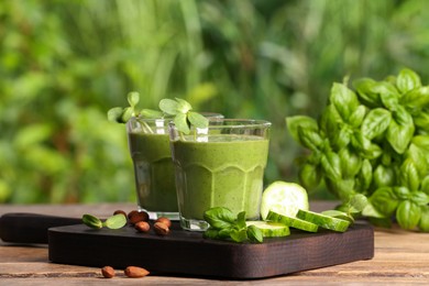 Glasses of fresh green smoothie and ingredients on wooden table outdoors