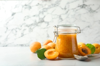 Photo of Jar of apricot jam and fresh fruits on light table. Space for text