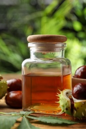 Chestnuts and jar of essential oil on table against blurred background