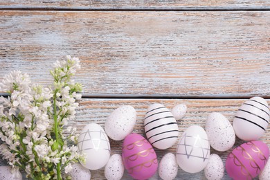 Photo of Many painted Easter eggs and branch of lilac flowers on rustic wooden table, flat lay. Space for text