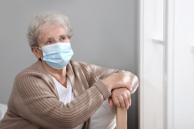 Lonely senior woman in protective mask sitting on bed at nursing home