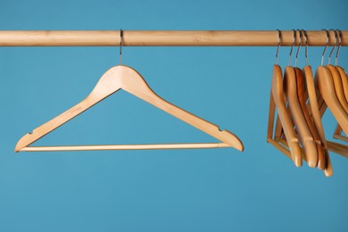 Empty clothes hangers on wooden rail against light blue background