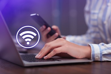 Woman using smartphone and laptop connected to WiFi at wooden table indoors, closeup
