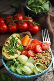 Delicious lentil bowl with avocado, tomatoes, carrot and cucumber on wooden table