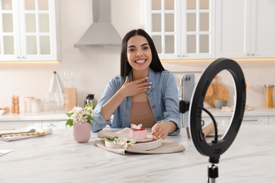 Blogger with tasty cake recording video in kitchen at home. Using ring lamp and smartphone