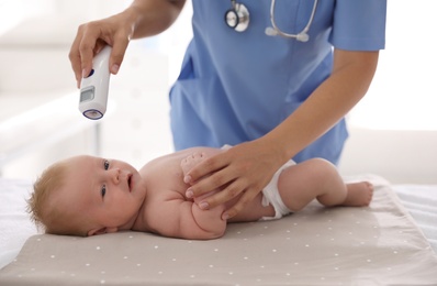 Doctor measuring temperature of little baby with non-contact thermometer in clinic, closeup. Health care