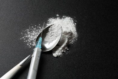 Spoon with cocaine powder and syringe on dark background. Space for text