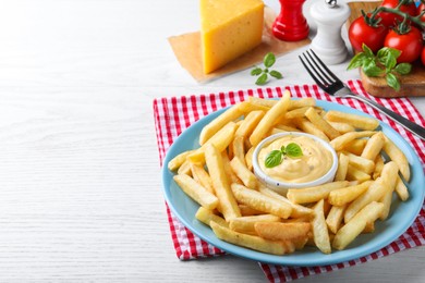 Delicious French fries and cheese sauce with basil on white wooden table, space for text