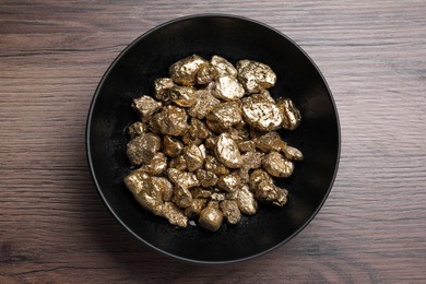 Bowl of gold nuggets on wooden table, top view