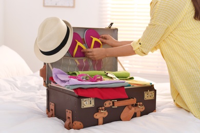 Woman packing suitcase for summer vacation in bedroom, closeup