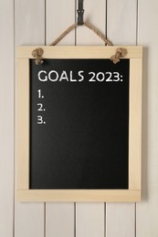 Blackboard with phrase GOALS 2023 and empty checklist on hanging on white wooden background