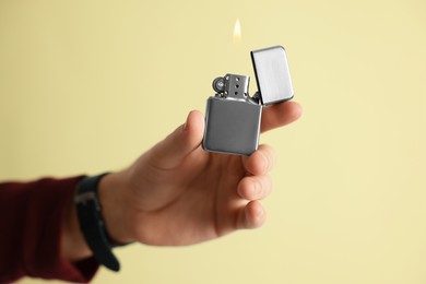 Photo of Man holding lighter with burning flame against beige background, closeup. Space for text