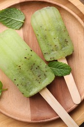 Tasty kiwi ice pops on wooden plate, top view. Fruit popsicle