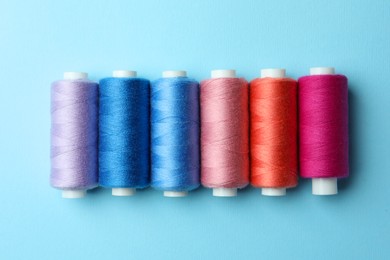 Photo of Set of different colorful sewing threads on light blue background, flat lay