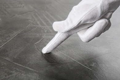 Person in white glove checking cleanliness of grey stone table, closeup