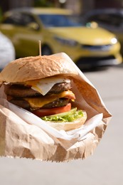 Delicious burger in paper wrap on city street, closeup