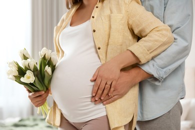 Young pregnant woman with flowers and her husband indoors, closeup