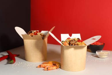 Boxes of wok noodles with seafood on color background