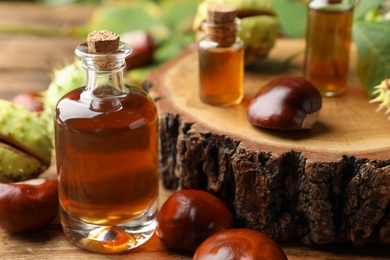Chestnuts and bottles of essential oil on wooden table, closeup