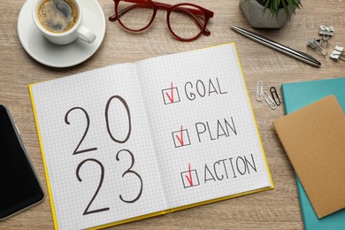Photo of Flat lay composition of notebook with text 2023 Goal, Plan, Action on wooden table. New year resolutions