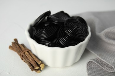 Tasty black candies and dried sticks of liquorice root on white table, closeup