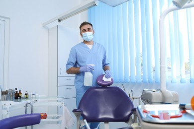 Professional dentist in uniform cleaning workplace  with antiseptic indoors