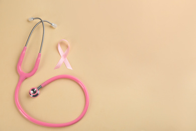 Pink ribbon and stethoscope on beige background, flat lay with space for text. Breast cancer concept