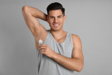 Handsome man applying deodorant to armpit on grey background