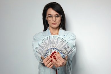 Portrait of stylish woman with money fan on light background