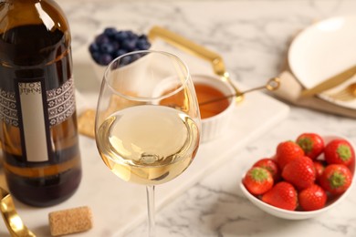 Glass of wine near bottle and delicious snacks on white table, closeup