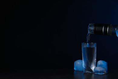 Pouring vodka from bottle in glass and ice cubes on black background. Space for text