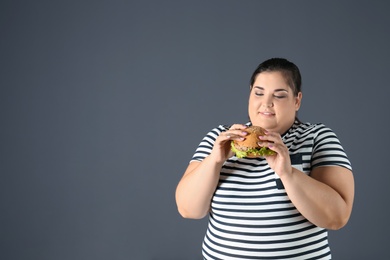 Overweight woman with hamburger and space for text on gray background